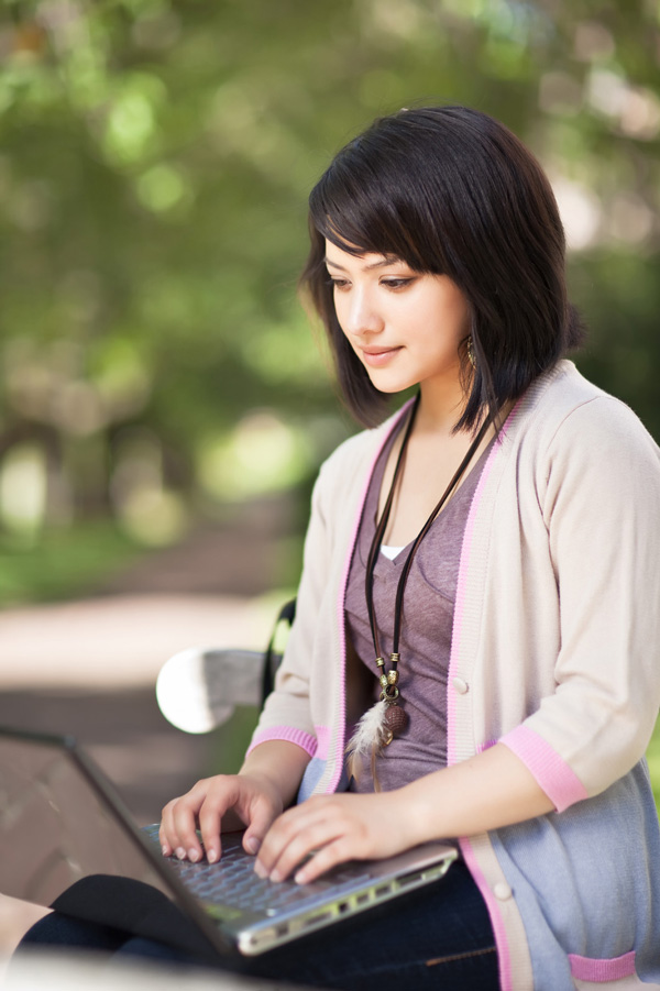 student on computer on park bench